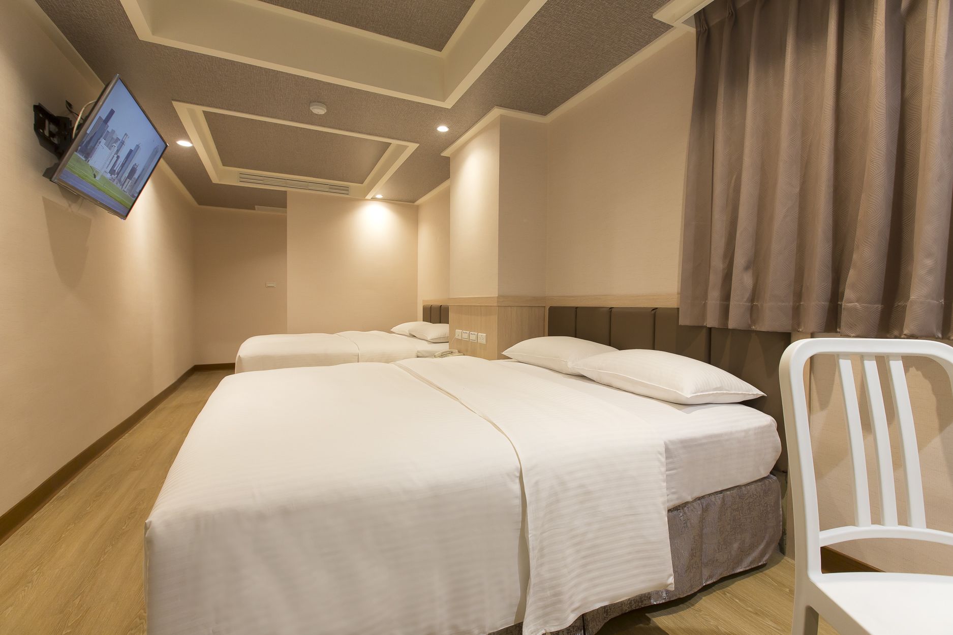 A hotel room with two beds, a television mounted on the wall, and a chair.