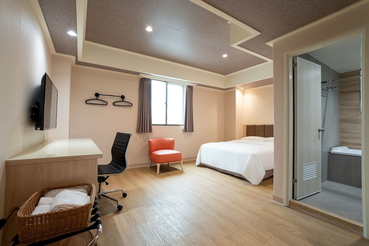 Une chambre d’hôtel comprenant un lit, un bureau, une chaise, une télévision, une fenêtre avec des rideaux et un espace douche.