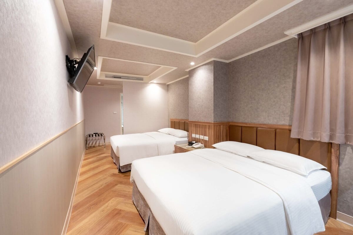 Une chambre d’hôtel avec deux lits, un téléviseur fixé au mur et une tête de lit en bois.