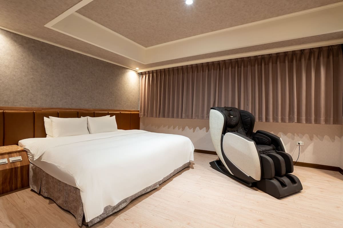 Une chambre d’hôtel avec un lit, un fauteuil massant et une table de chevet en bois.