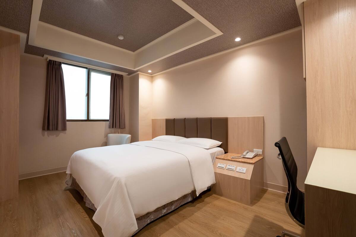 Une chambre d’hôtel avec un grand lit, un bureau avec un téléphone et une chaise.