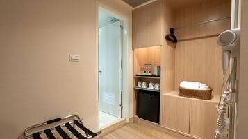 A hotel bathroom with a shower, a hairdryer, a towel, and a small shelf with toiletries.