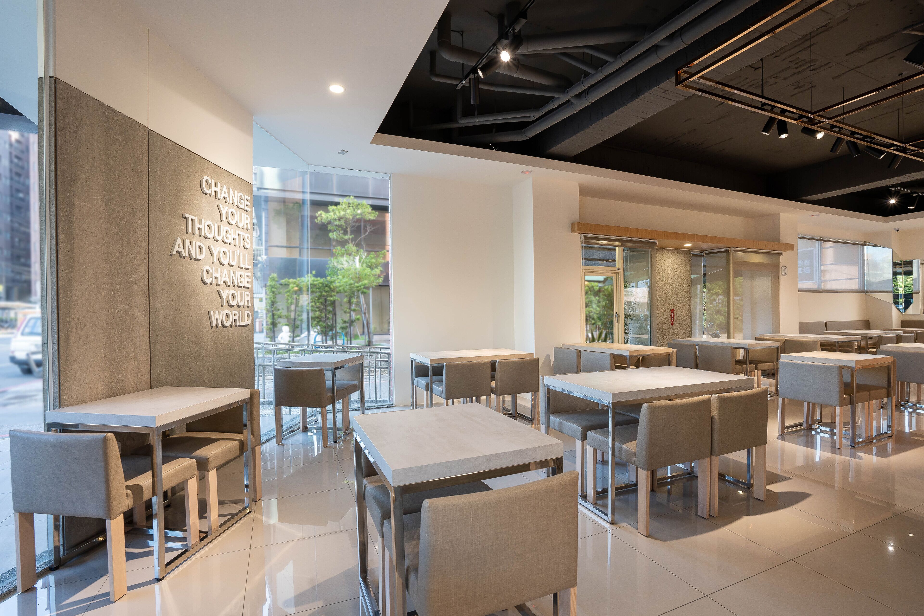 Un café moderne doté de nombreuses tables et chaises, de grandes fenêtres et d’inscriptions inspirantes sur les murs.