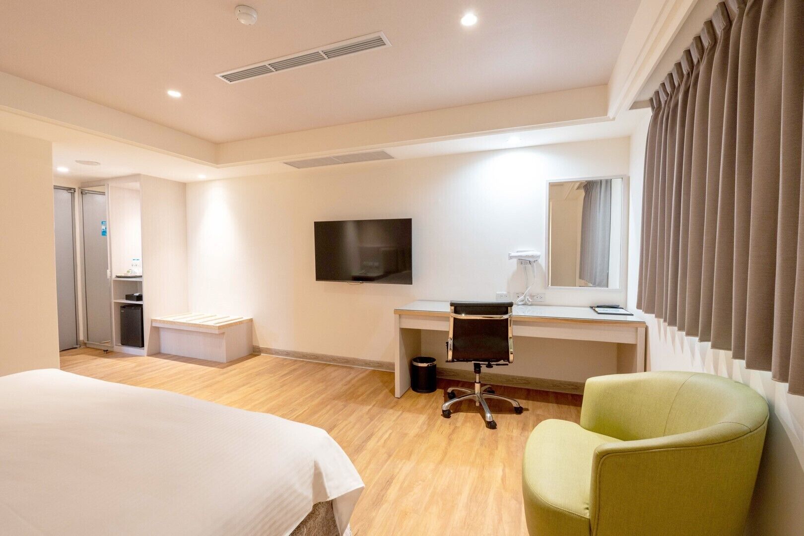 A hotel room with a bed, a desk, a chair, a TV, and a window with curtains.