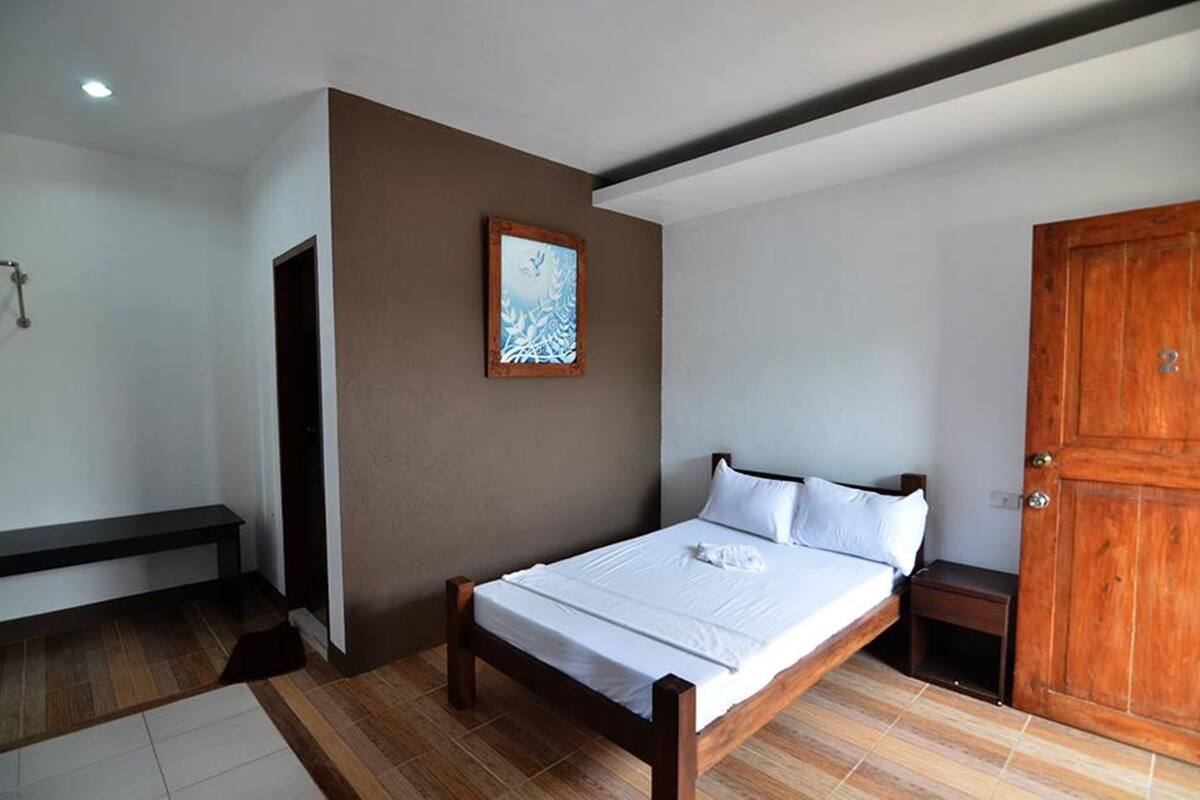 A bedroom with a wooden bed, a bench, a wooden door, and a framed picture on the wall.
