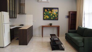 A modern kitchen with a built-in stove, a dining area with a table, and a green sofa in a living room. - Kemang Inn (Jakarta)