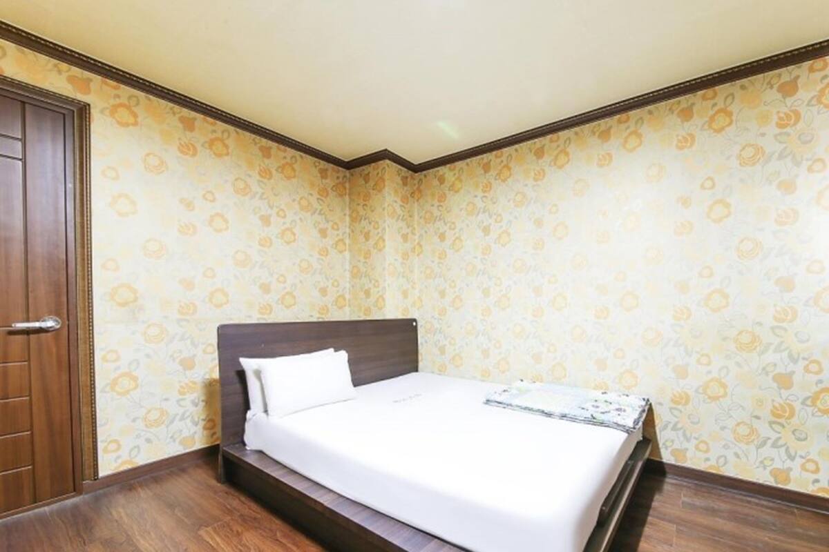 Een slaapkamer met een houten bed, een witte matras en een behang met een bloemenmotief.