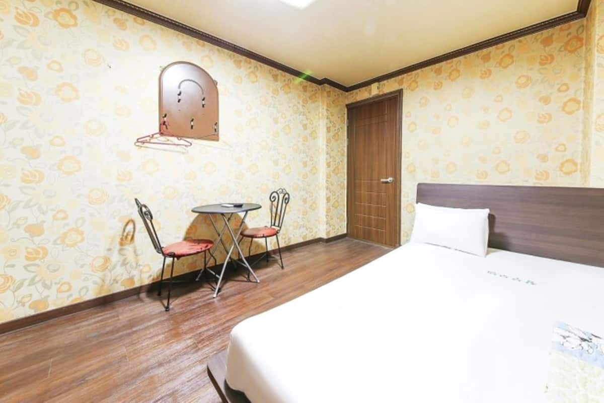 Hotelkamer met een bed, twee stoelen, een kleine tafel, een houten deur en een wandlamp.