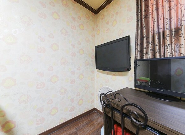 A room with a TV mounted on the wall, a wooden desk, and a chair.