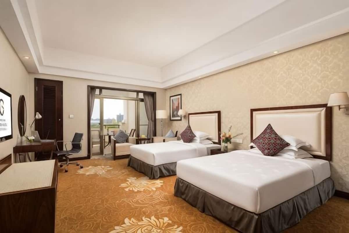 Een hotelkamer met twee bedden, een bureau, een stoel, een bureaulamp en uitzicht op de omgeving.