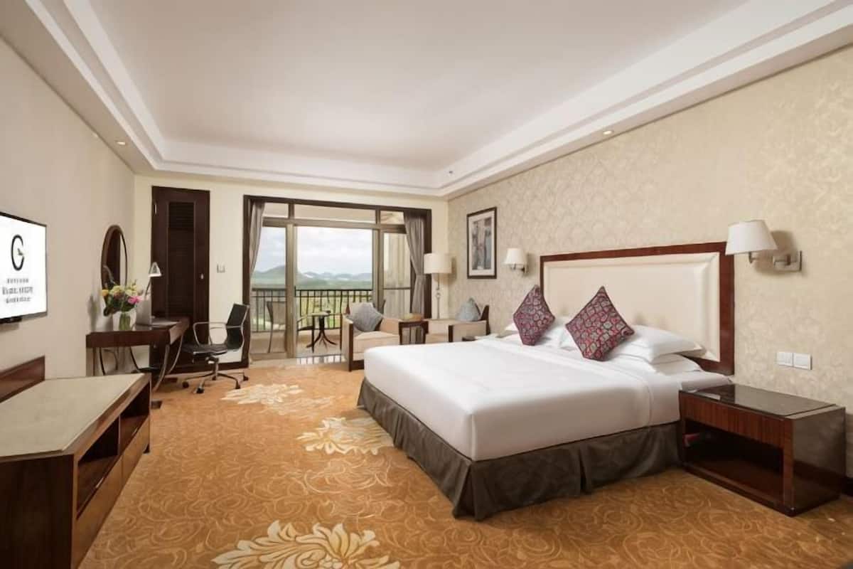 Hotelkamer met een groot bed, een bureau, een stoel, een nachtkastje en een balkon met uitzicht.