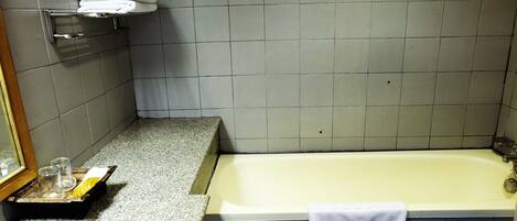 A bathroom with a bathtub, a towel rack with folded towels, a tray with glasses and a yellow object, and a mirror on the wall.