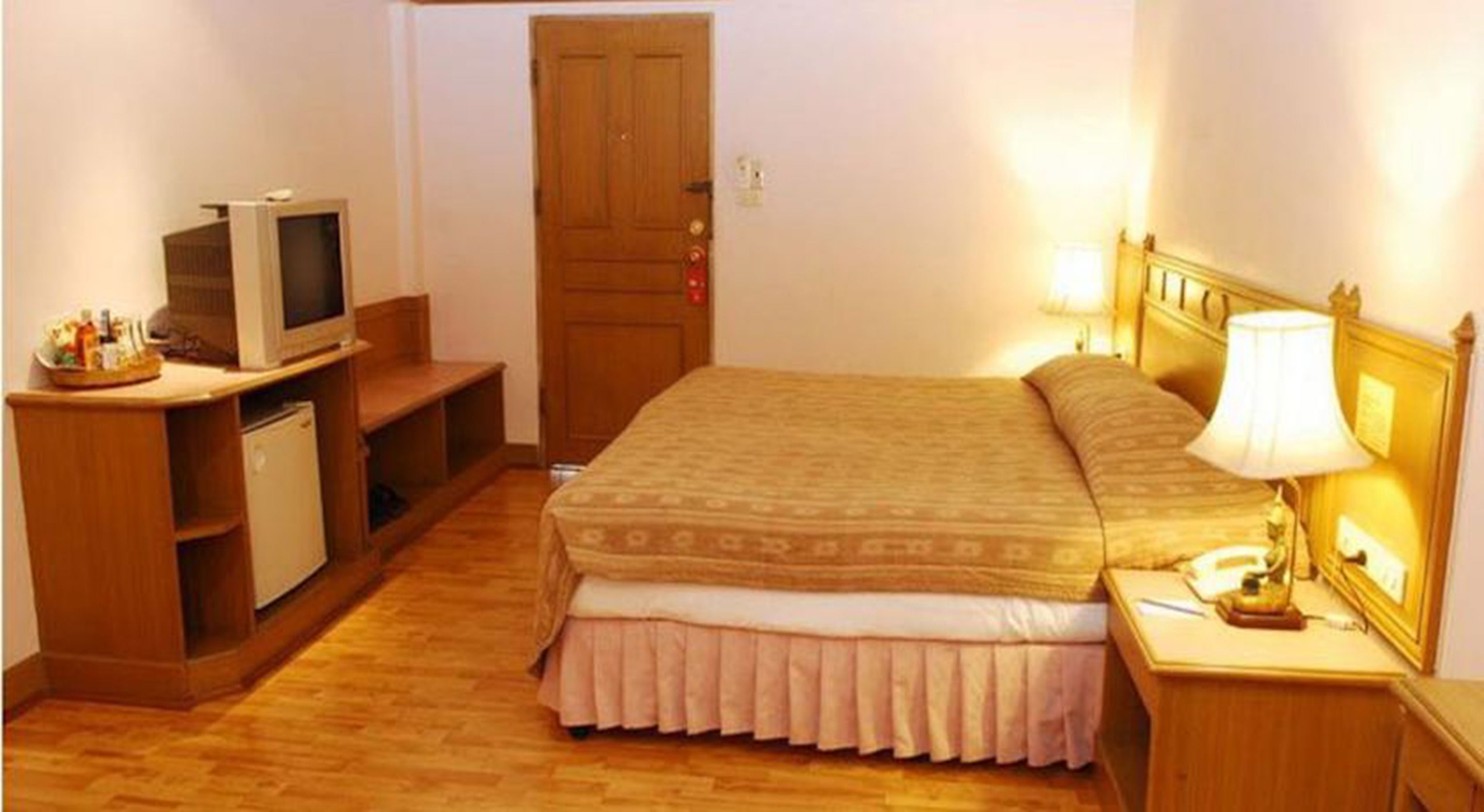 A bedroom with a bed, a television, a desk, and a lamp.