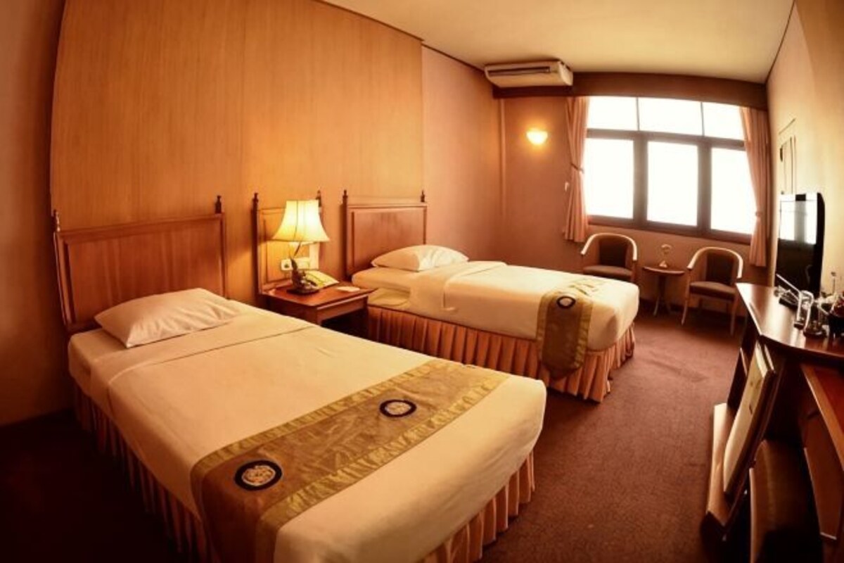 A hotel room with two beds, a desk, a chair, a TV, and a window.