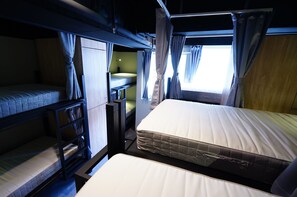 A bunk bed room with a window, curtains, and a bedside table.