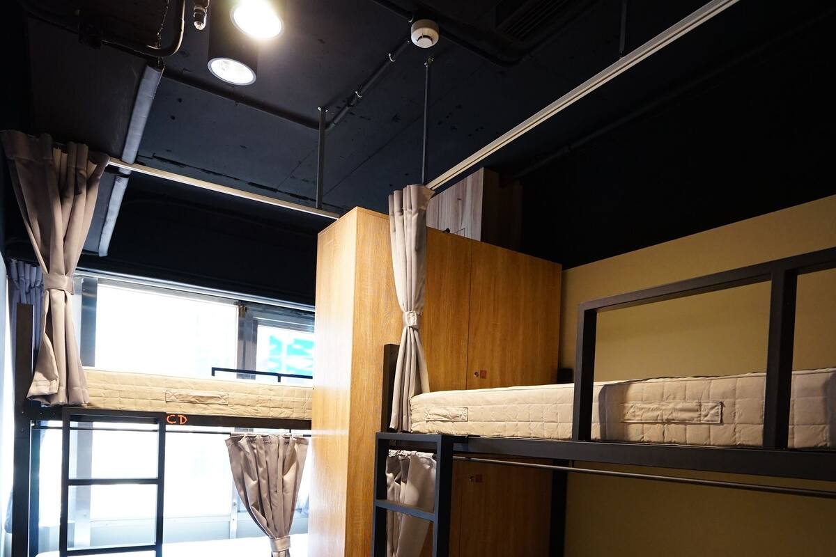 A bunk bed room with a window, curtains, and a wooden wardrobe.