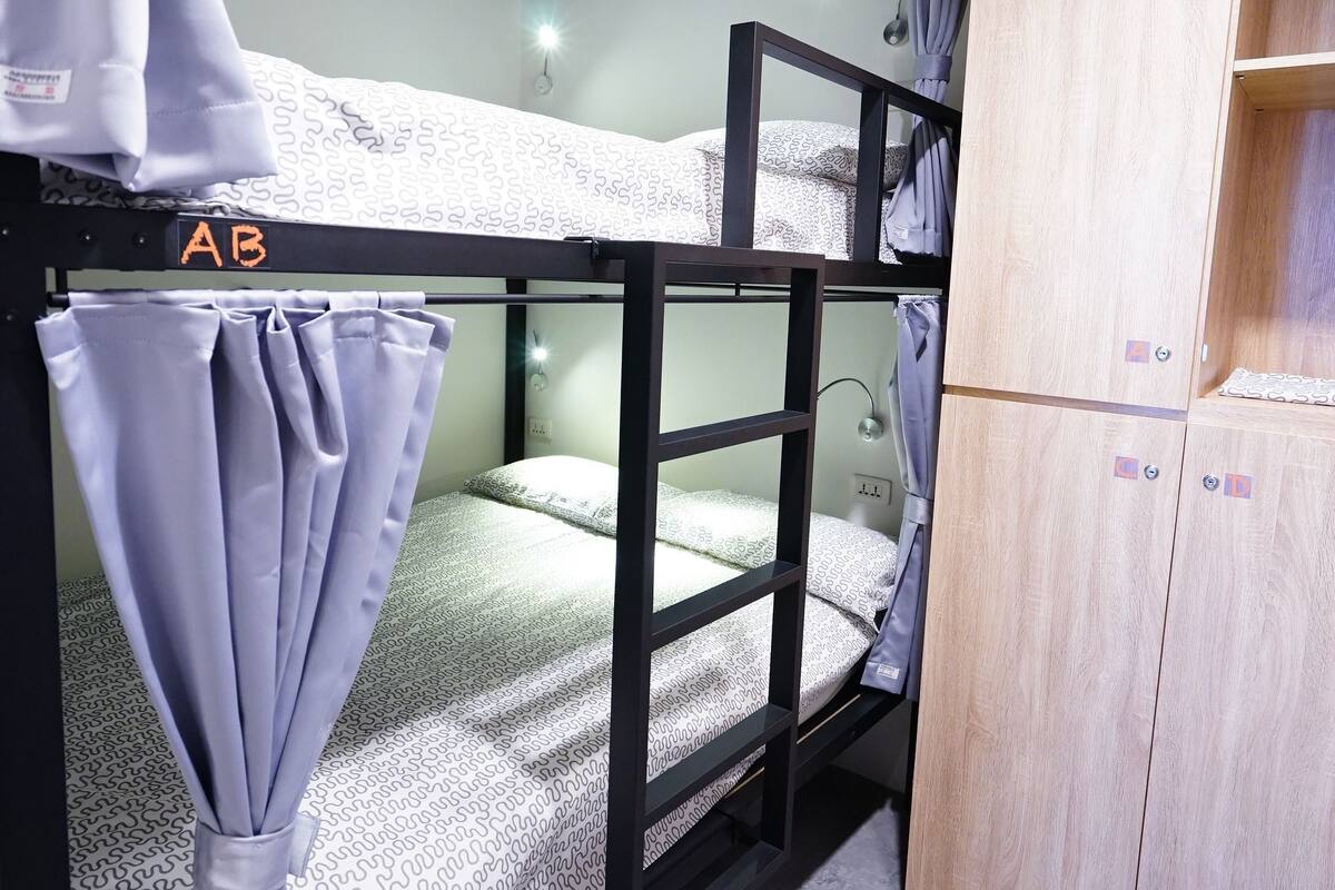 A bunk bed with a curtain, a wooden wardrobe, and a desk lamp.