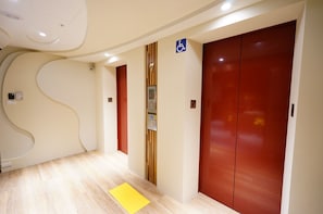 Corredor com piso de madeira, um tapete amarelo e duas portas vermelhas com o sinal azul de acessibilidade.
