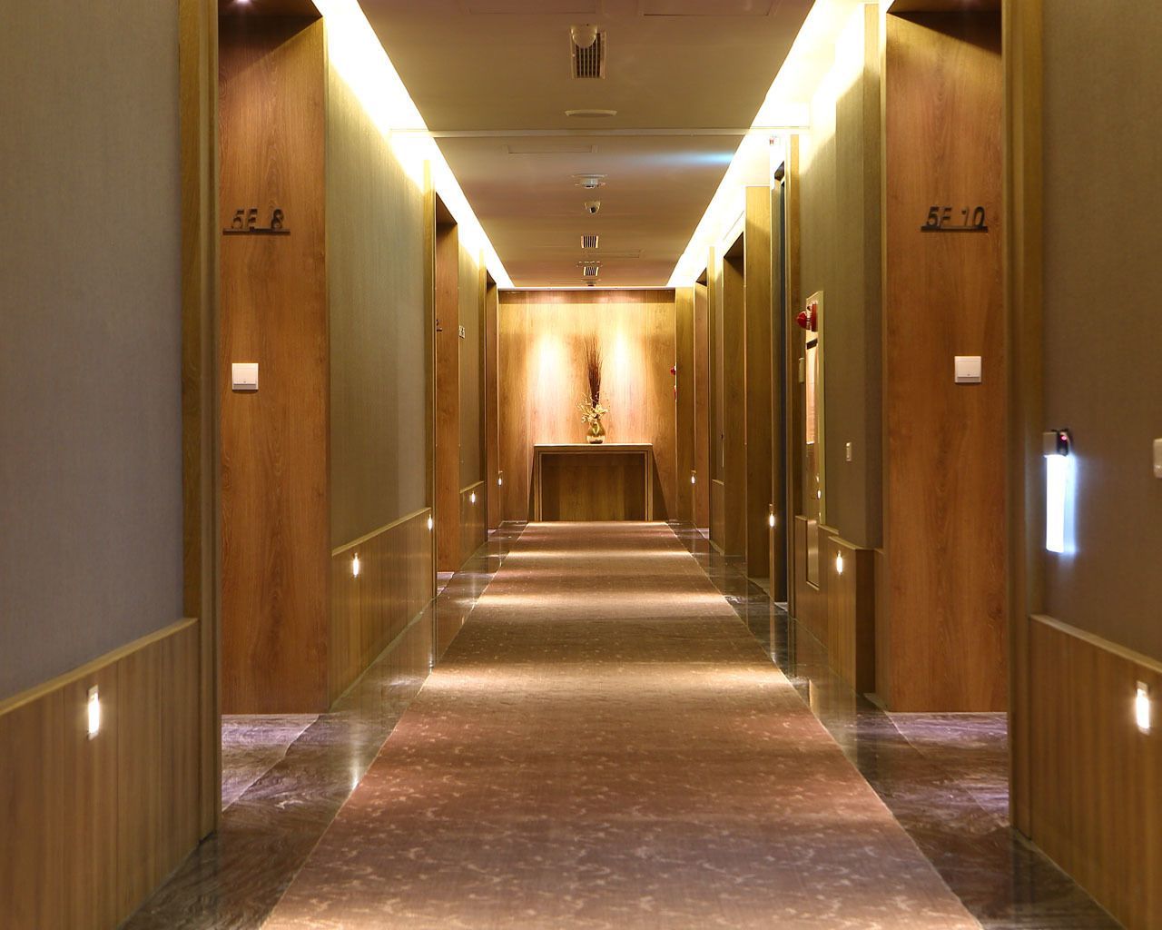 A hotel corridor with wooden paneling, a marble floor, and illuminated wall sconces.