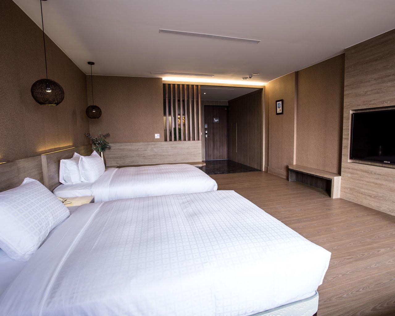 Habitación de hotel con dos camas, un televisor de pantalla plana, suelo de madera y diseño moderno.