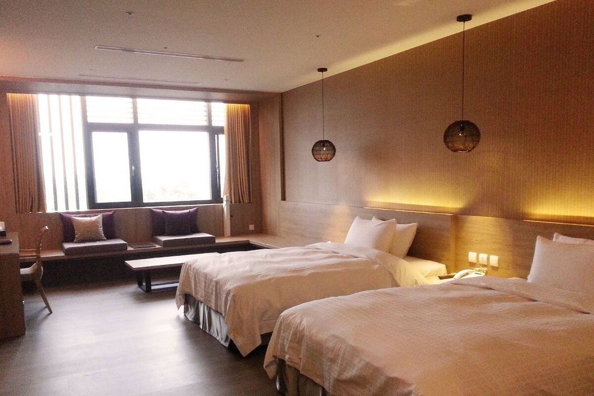 Une chambre d’hôtel avec deux lits, un canapé, un bureau et une grande fenêtre avec des rideaux.