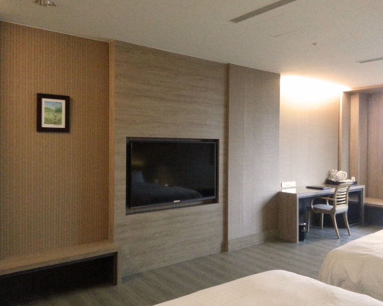 Habitación de hotel con una televisión de pantalla plana grande montada en la pared, un escritorio con una silla y una cama.