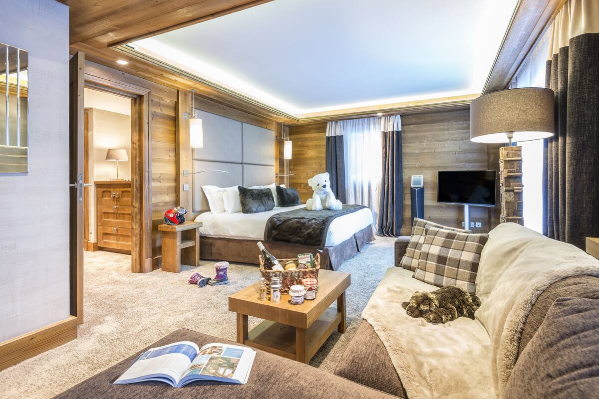 Habitación de hotel bien iluminada con cama, sofá, mesa de centro y televisor.