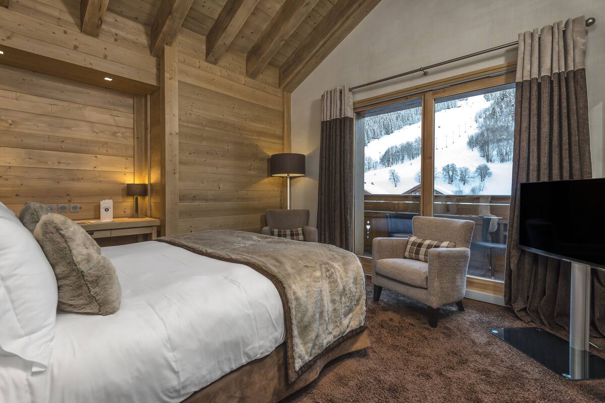 Un dormitorio con una cama grande, una silla, un televisor y una ventana que ofrece vistas a un paisaje nevado.