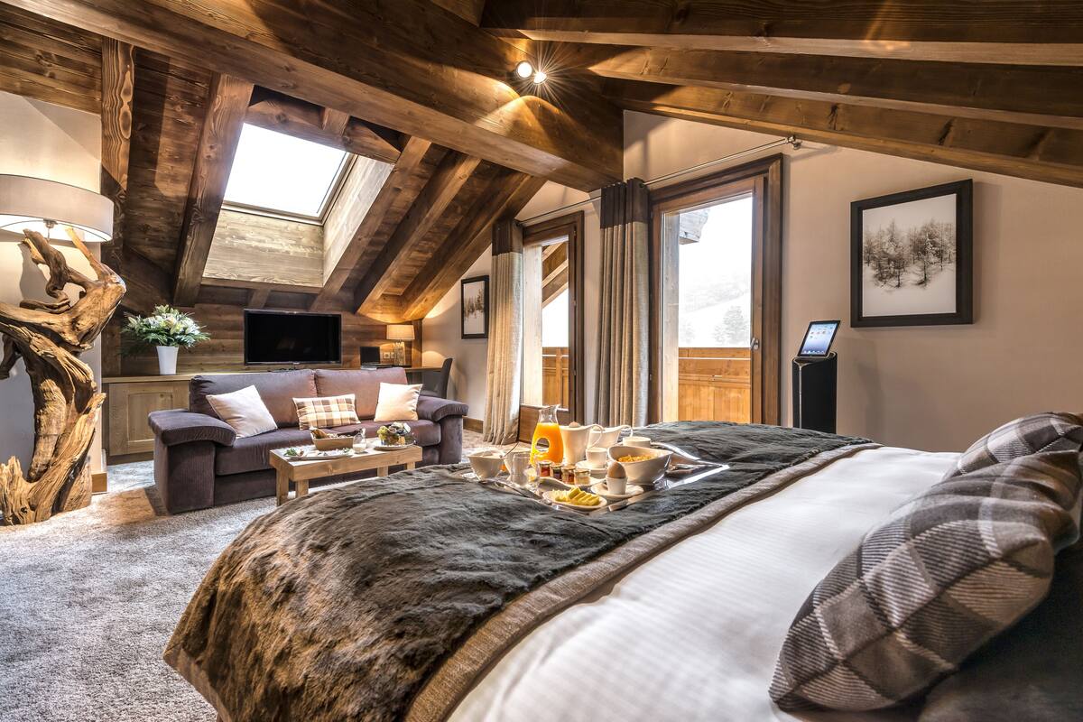 Un dormitorio acogedor y rústico con una cama grande, techo de madera, tragaluz, sofá y una mesa de comedor con alimentos para el desayuno.