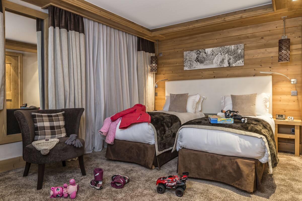 Un dormitorio con dos camas, una silla y una pared de madera.