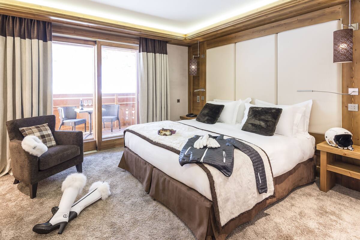 Habitación de hotel con una cama grande, una silla, un par de esquíes y un balcón con mobiliario exterior.