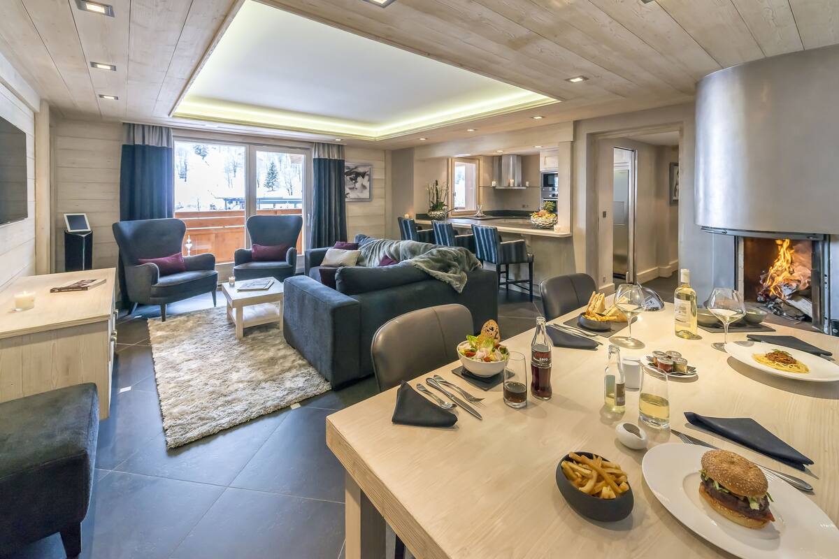 Una sala moderna con comedor, chimenea y cocina al fondo.
