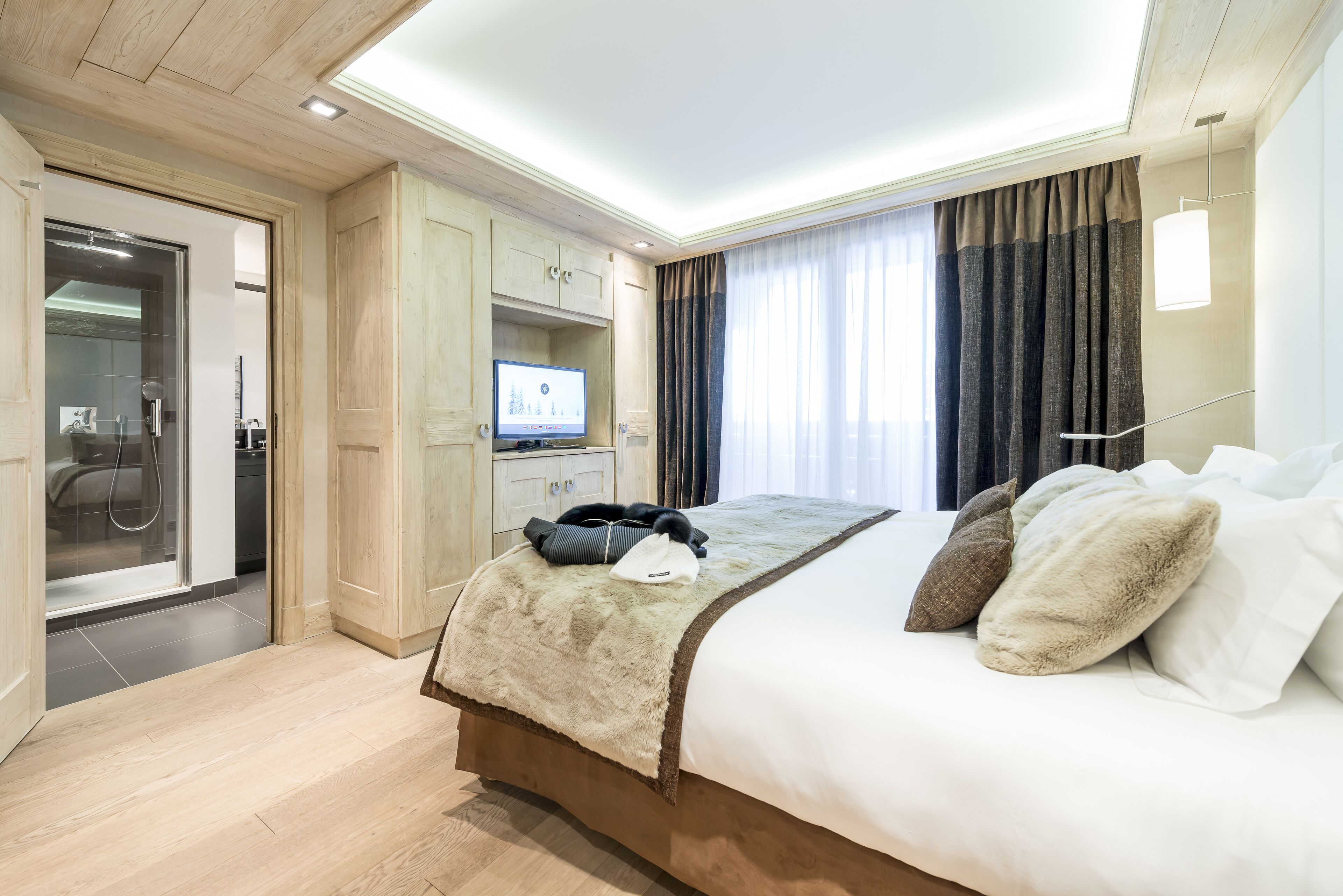Una habitación de hotel moderna con una cama grande, televisión, armario y baño visible a través de una puerta abierta.