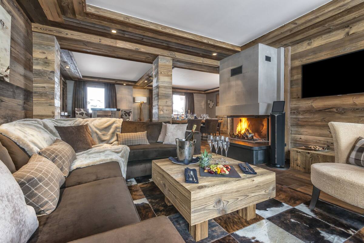 Un salón acogedor con chimenea, vigas de madera, un sofá y una mesa de centro con aperitivos.