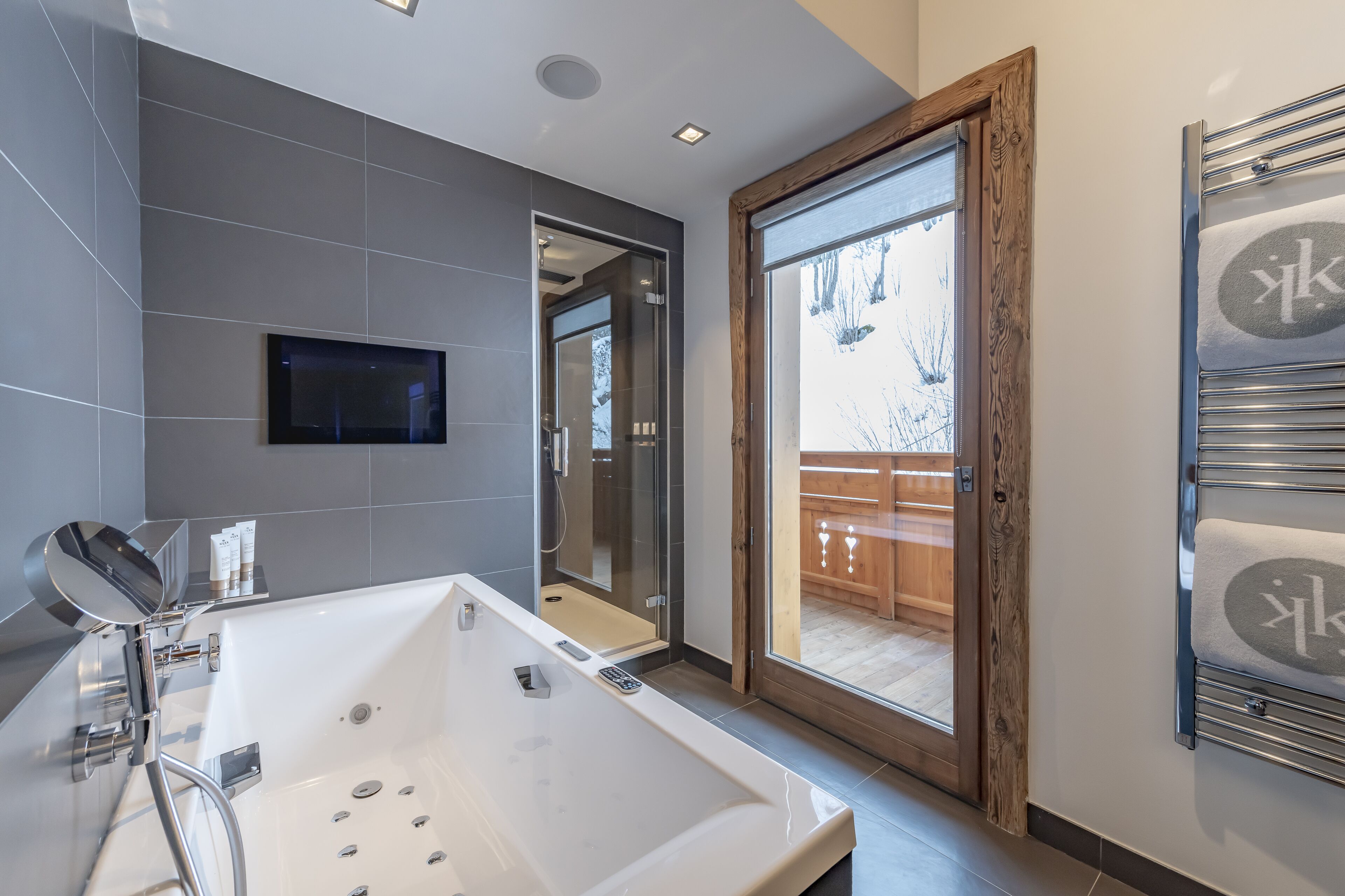 A modern bathroom with a large bathtub, a glass shower enclosure, and a sliding glass door leading to a balcony.