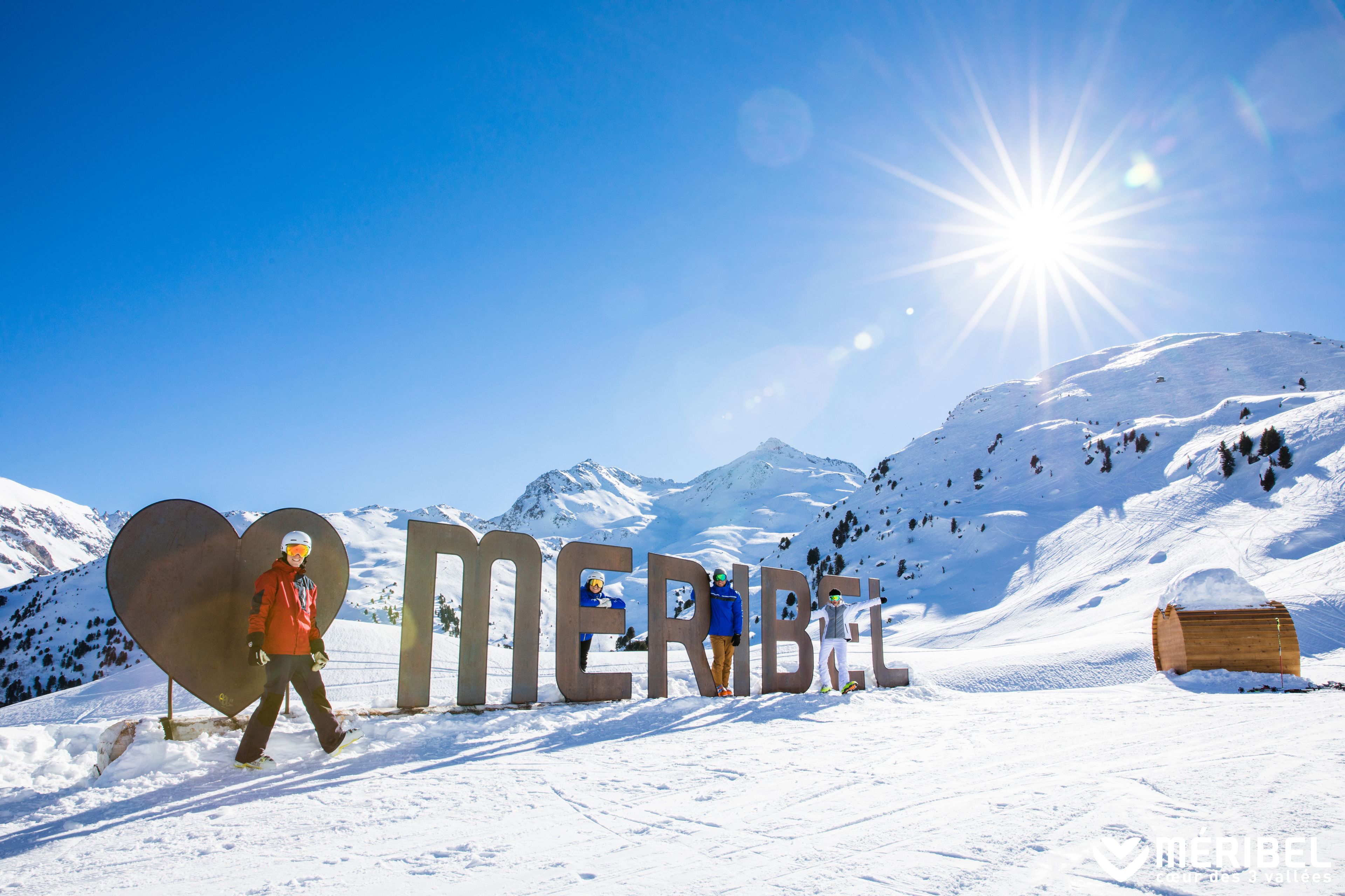 A snowy mountain scene with large letters spelling "MERIBEL" and a person walking in the foreground.