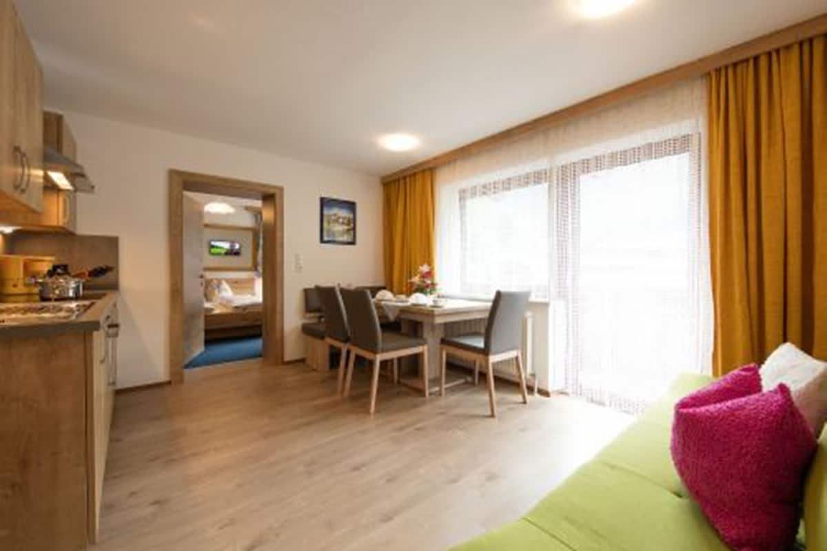 A compact living space with a dining area, kitchenette, and a green sofa with a pink pillow.