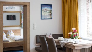 Una habitación con cama, una mesa y sillas, un cuadro enmarcado y una ventana con cortinas.