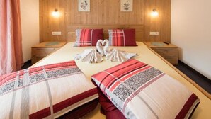 Una cama doble con una disposición de toallas en forma de corazón, cabecera de madera, dos mesitas de noche e iluminación de pared.