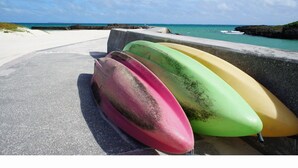 Tres kayaks coloridos alineados sobre una superficie de concreto cerca de la playa.