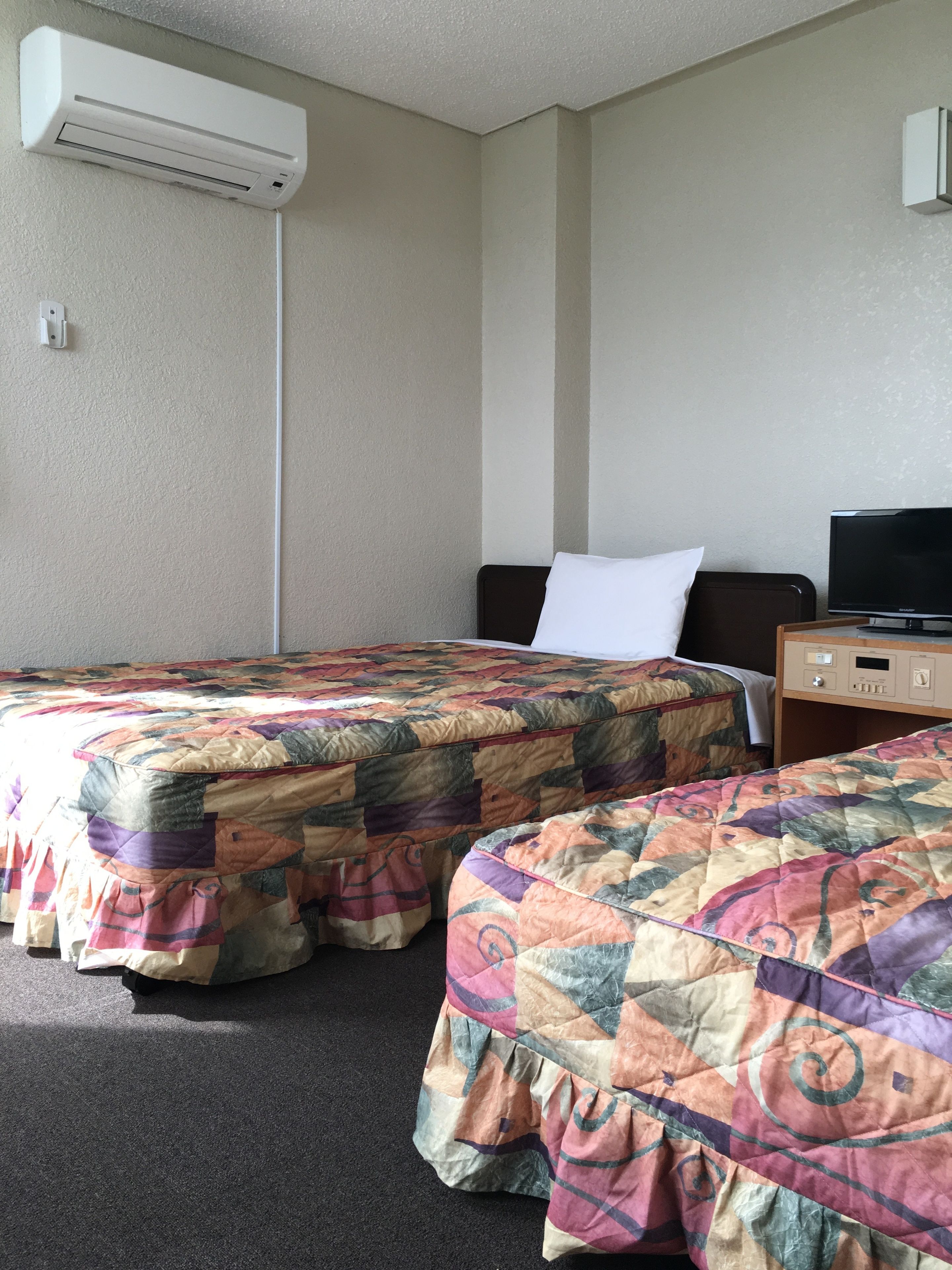 A hotel room with two beds, a TV, and an air conditioning unit.