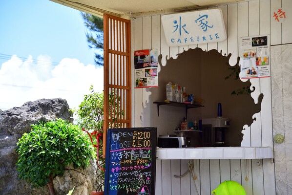 Un café à la façade en bois, avec un panneau affichant le menu et un tableau noir indiquant les heures d’ouverture.