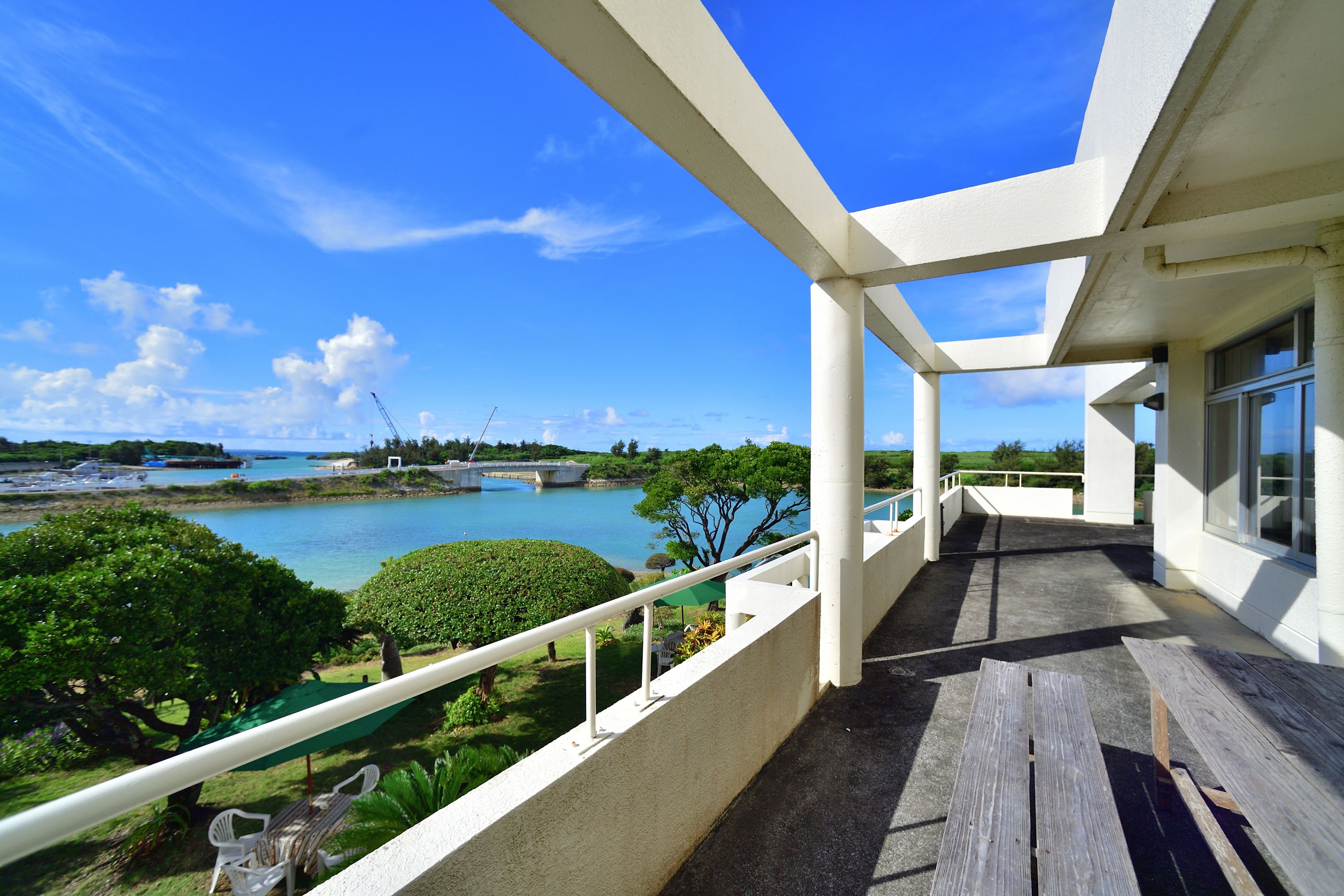 A balcony with a view of a body of water, greenery, and a distant bridge.