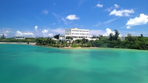 Un hotel costero con un edificio grande, vista a la playa y abundante vegetación.