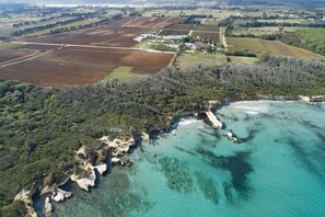 An aerial view of a coastal area with agricultural fields, a small settlement, and a rocky coastline. - Masseria Mongiò dell'Elefante (Otranto)
