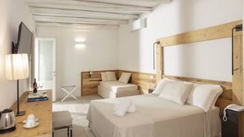 A hotel room with a wooden headboard, a bed with white linens, a bedside table with a lamp, a small table with a kettle, and a chair.
