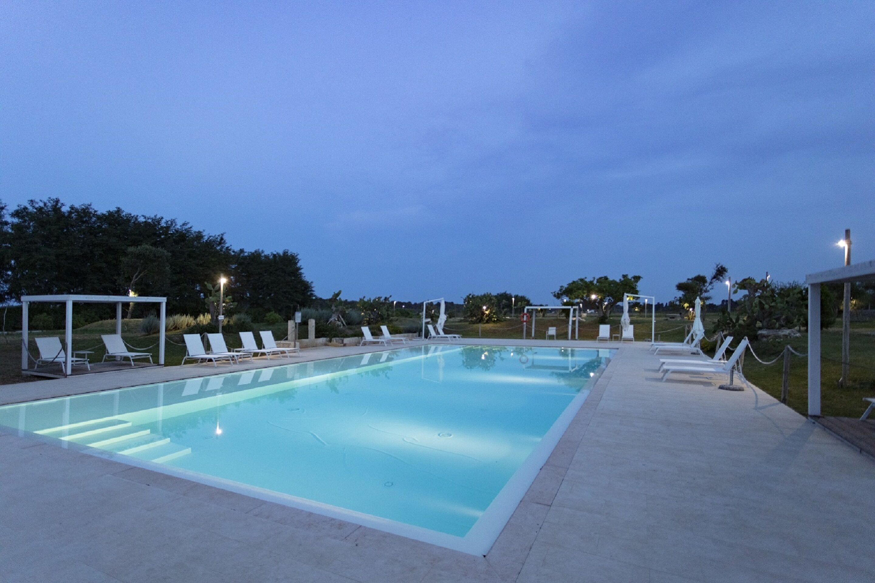 A rectangular swimming pool with a tiled deck and lounge chairs.