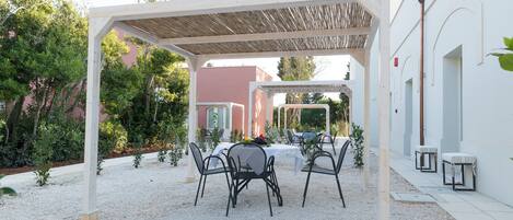 Um pátio externo com pérgola, mesas e cadeiras.
