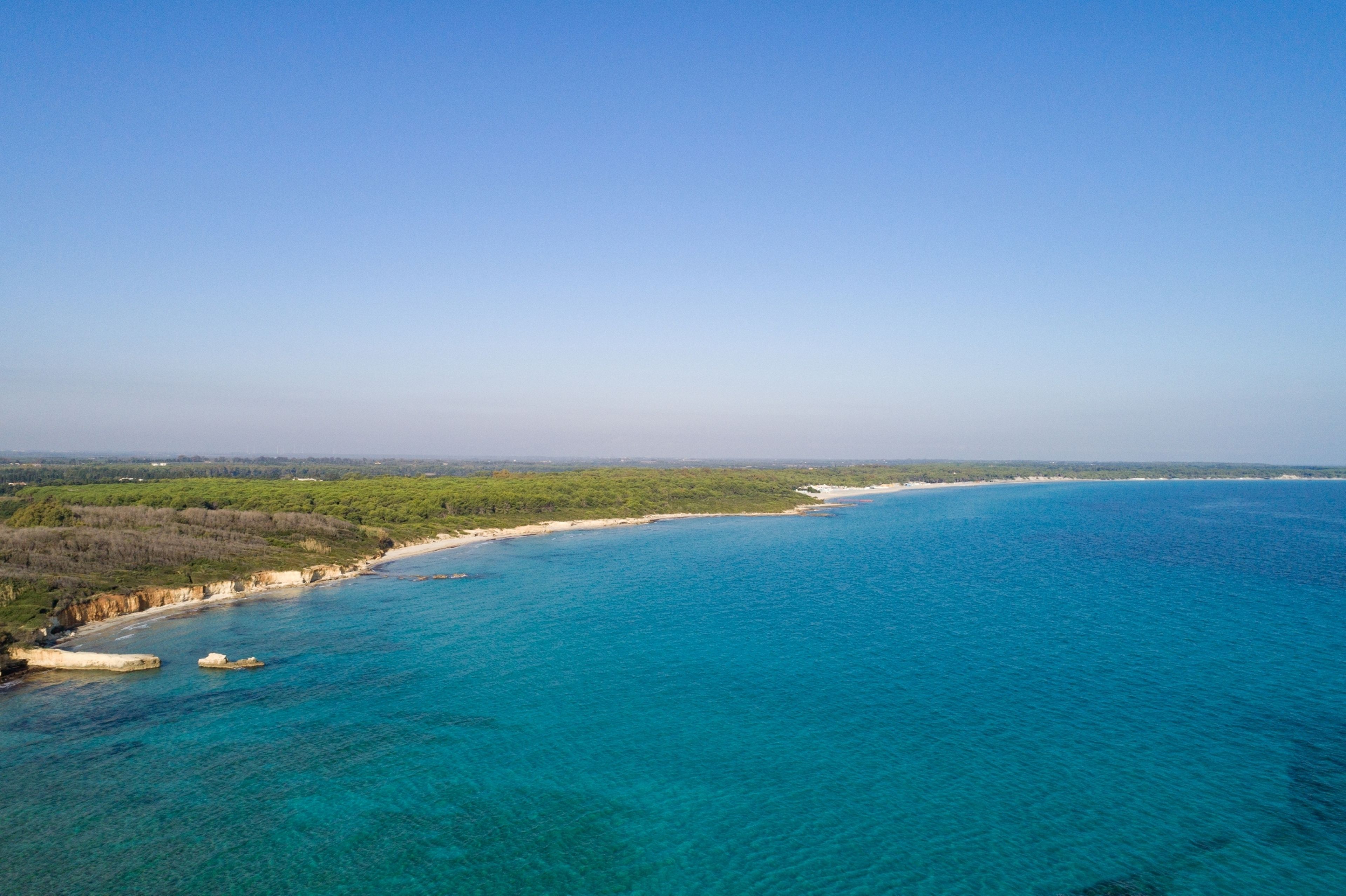 Vista aérea de una zona costera con aguas azules cristalinas, playas de arena y vegetación verde.