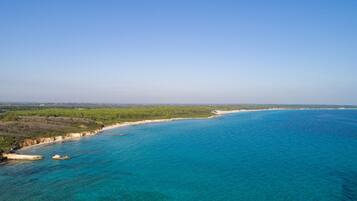 Vista aérea de una zona costera con aguas azules cristalinas, playas de arena y vegetación verde.